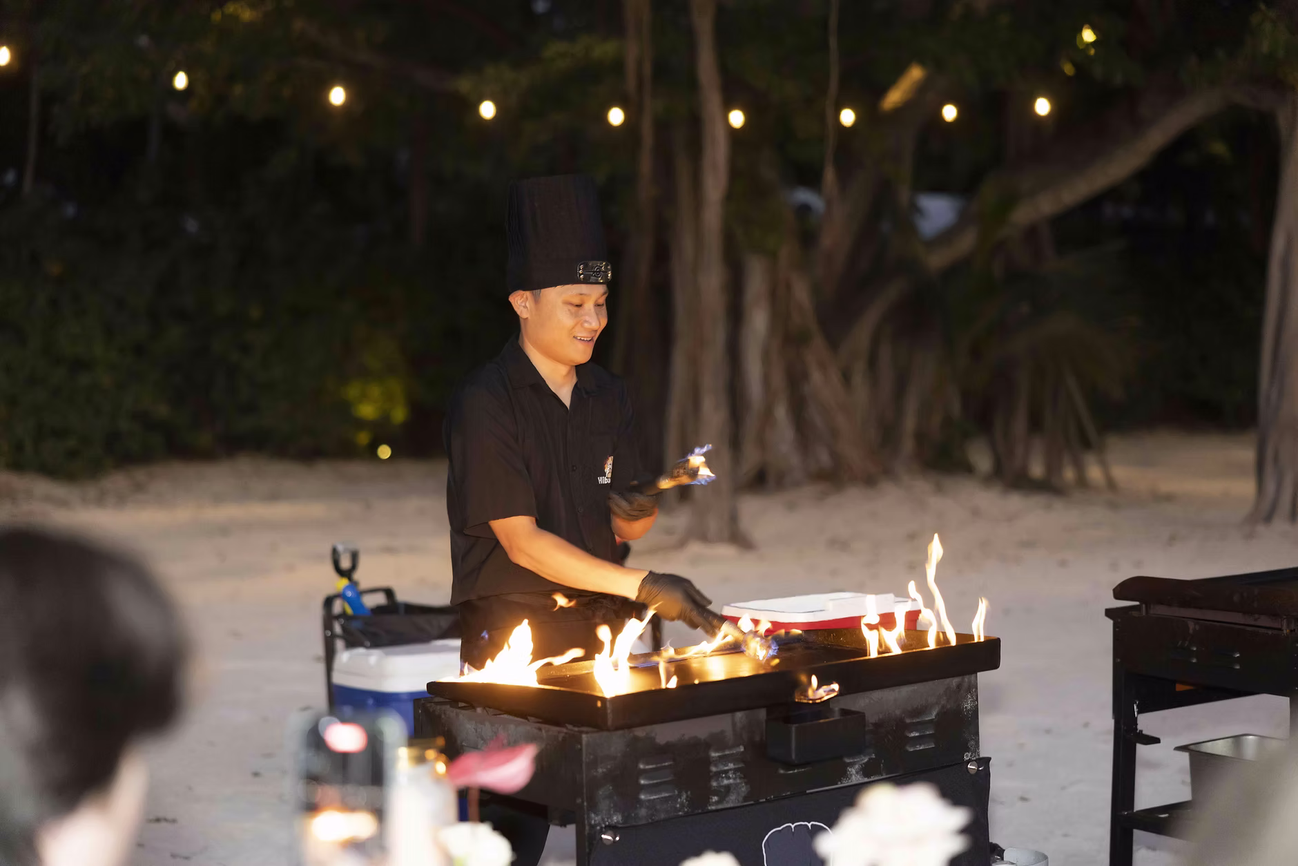 A hibachi chef cooking at an outdoor dinner under string lights